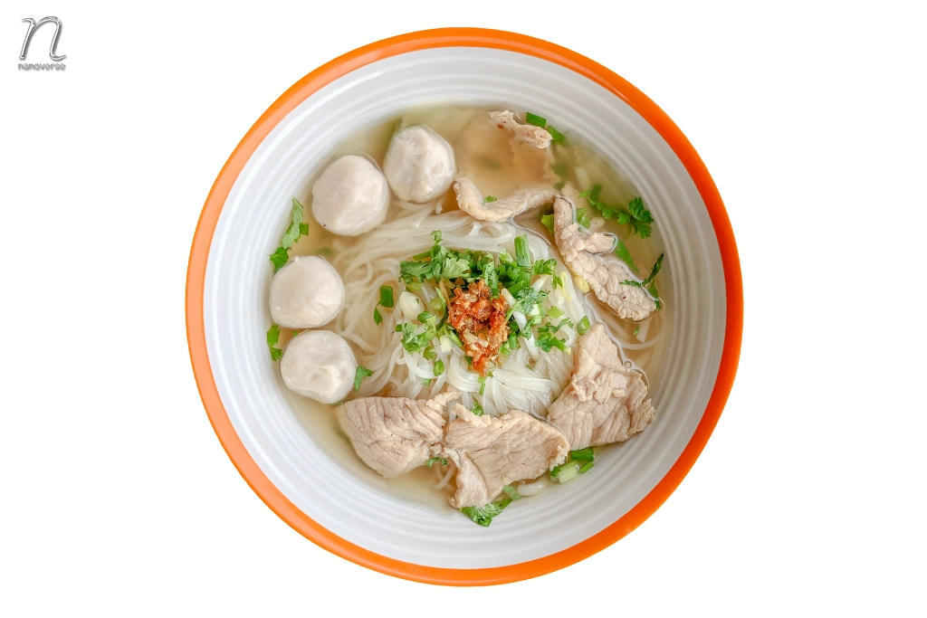 ชามก๋วยเตี๋ยวเสิร์ฟพร้อมเนื้อหมู ลูกชิ้น ต้นหอม และกระเทียมเจียวในน้ำซุปใส